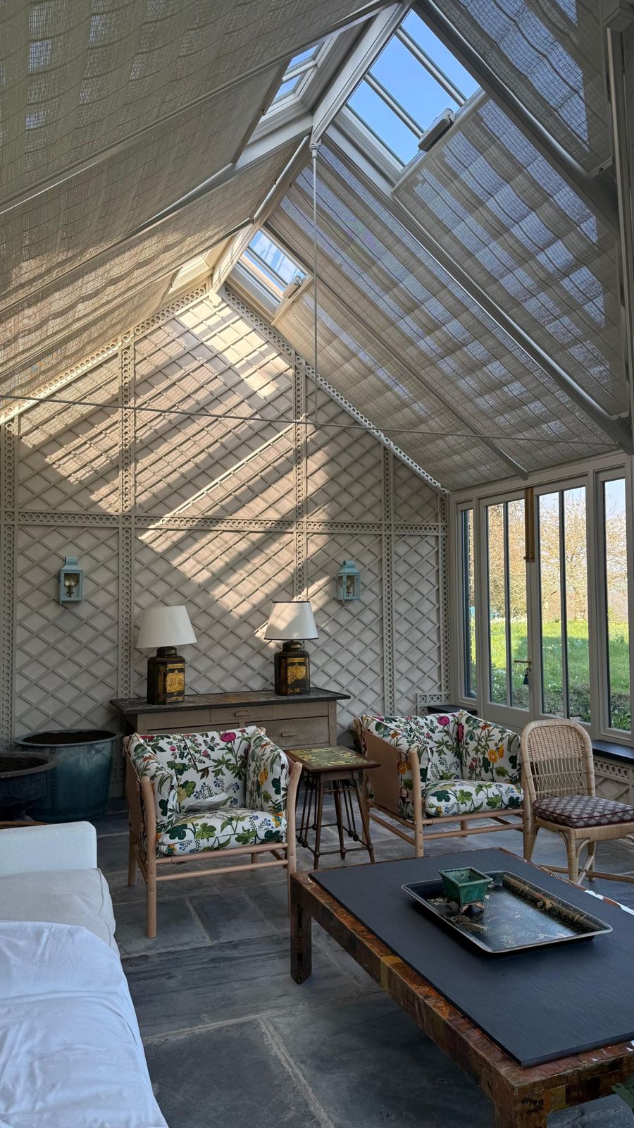 The new conservatory lined with trellis, with slate floor, linen blinds under the glass and garden chairs