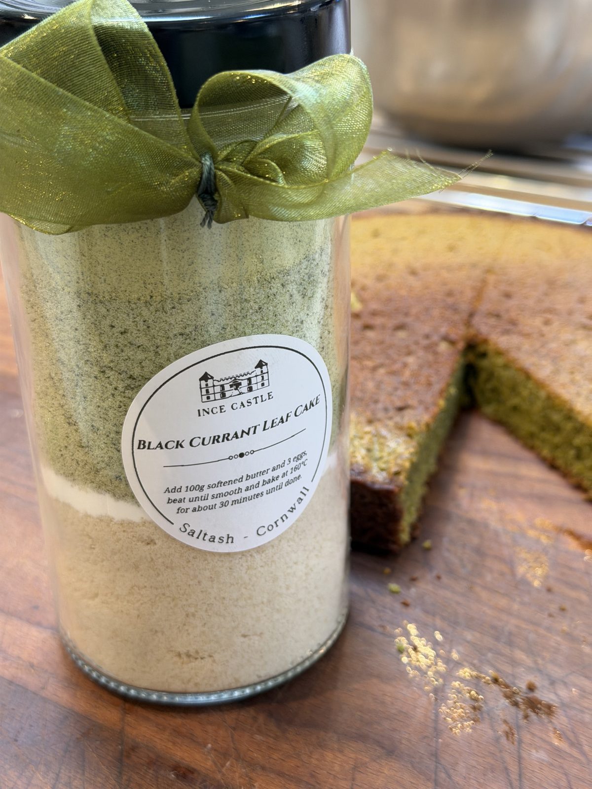 A jar of blackcurrant leaf cake mix tied with a green ribbon, beside a slice of the cake