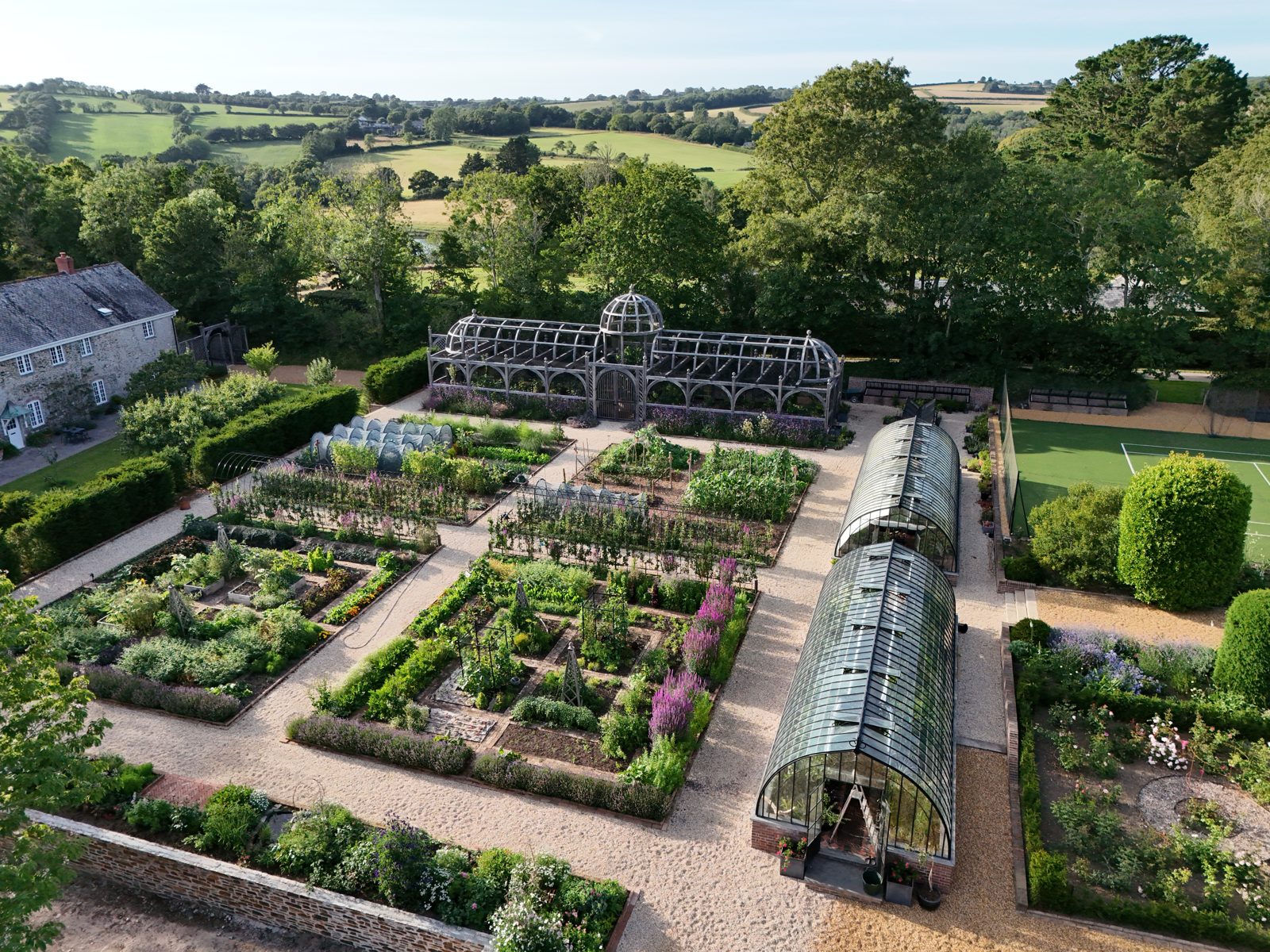 The walled kitchen garden from the air in July: beds of vegetables and flowers, the fruit cage, the long glasshouse and the fields beyond