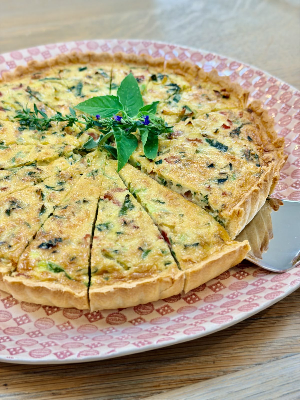 A quiche on a patterned plate, with herbs and flowers on top