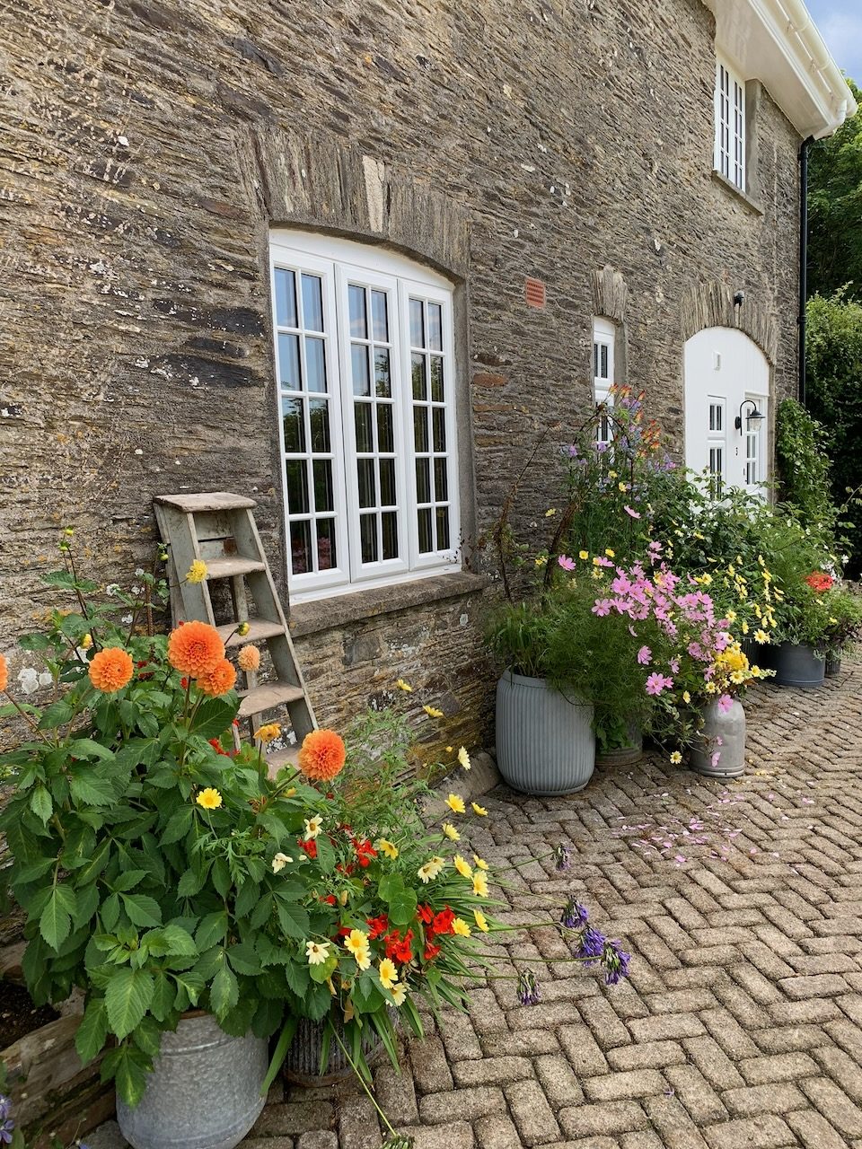 The front of the cottage, with pots of dahlias and cosmos on the brick path